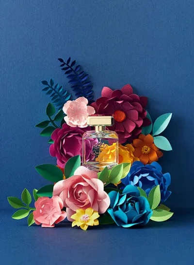 An elegant perfume bottle surrounded by colorful paper flowers, showcasing creative and artistic product photography for fragrance brands.