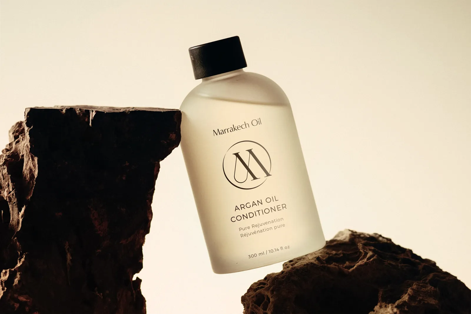 The Argan Oil Conditioner bottle from Marrakech Oil, staged on natural dark rocks to showcase its connection to earthy elements.