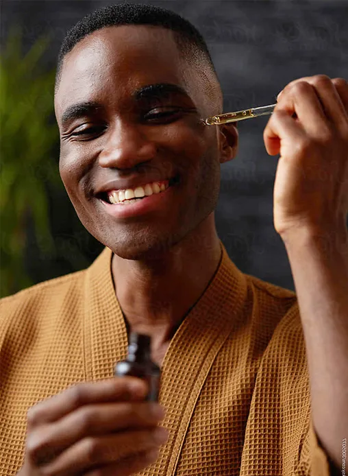 A man smiling while applying a facial serum, representing the growing market for men's skincare and grooming brands.